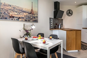 A modern kitchen with a central island, a dining table with chairs, and a cityscape painting on the wall.