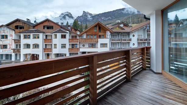 A balcony with wooden railings overlooking a row of buildings with balconies and a mountainous backdrop.