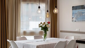 A dining area with a table set for six, white chairs, a vase with flowers, and pendant lights.