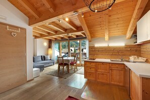 Una cocina moderna con vigas de madera, un área de comedor con sofá y sillas, y vistas a través de amplios ventanales.