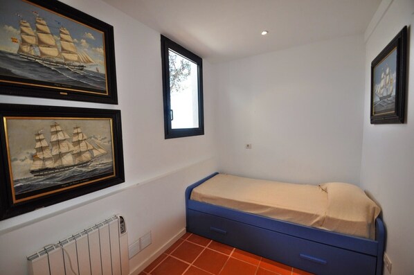 A small room with a single bed, two framed paintings of sailing ships, a window, and a radiator.