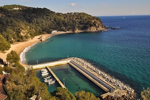A coastal area with a beach, a pier, boats, and a building on a hill.