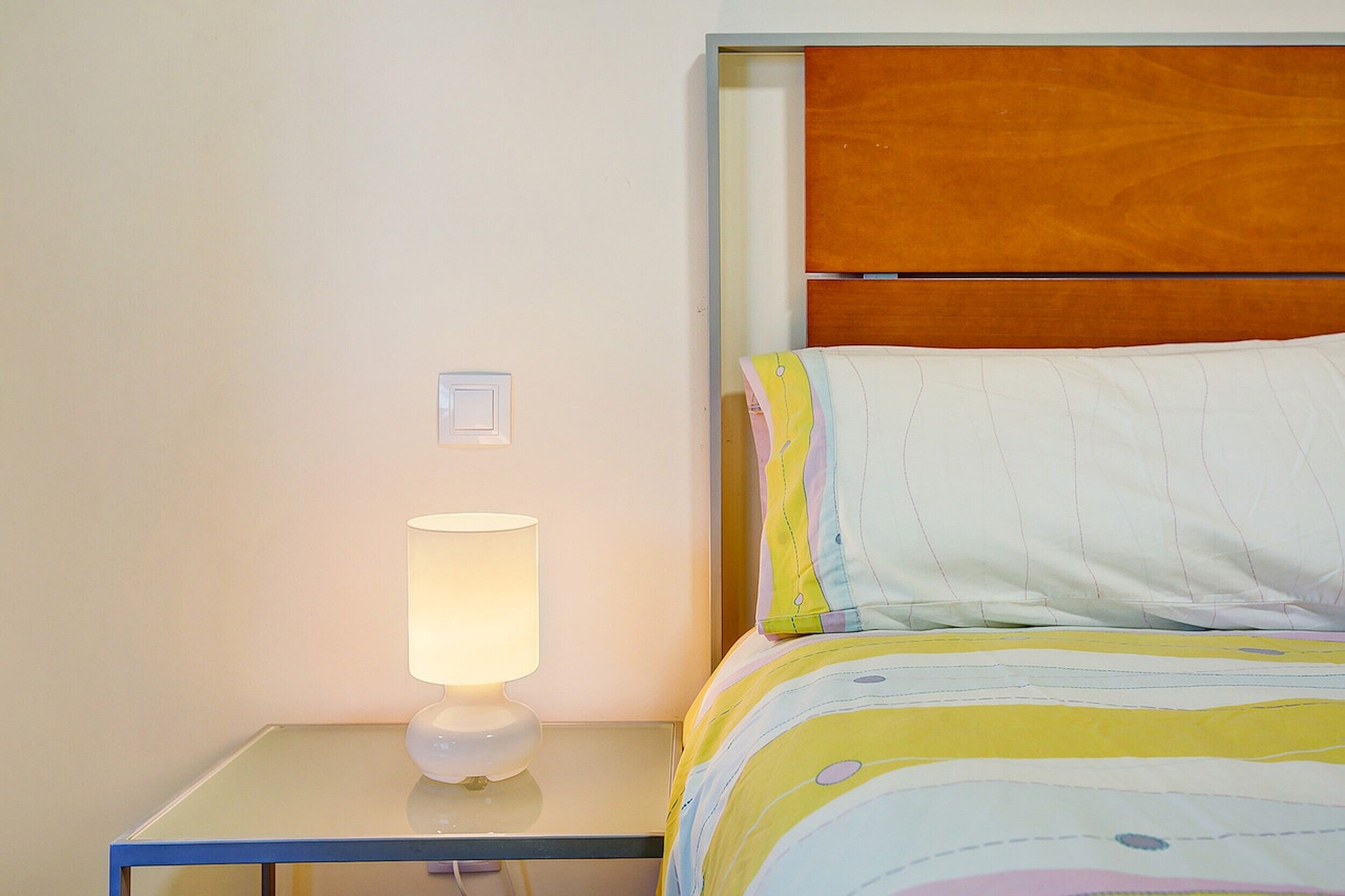 Un lit avec une couverture colorée, une table de chevet avec une lampe et une tête de lit en bois.