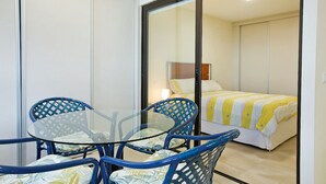 Ein Zimmer mit Glastisch und blauen Stühlen, ein Bett mit gestreifter Decke und eine Schiebetür.