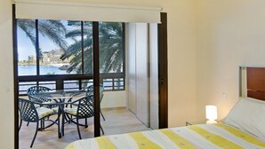 Ein Hotelzimmer mit Balkon, einem Bett, einem Tisch mit Stühlen und Blick auf Palmen und Gebäude.
