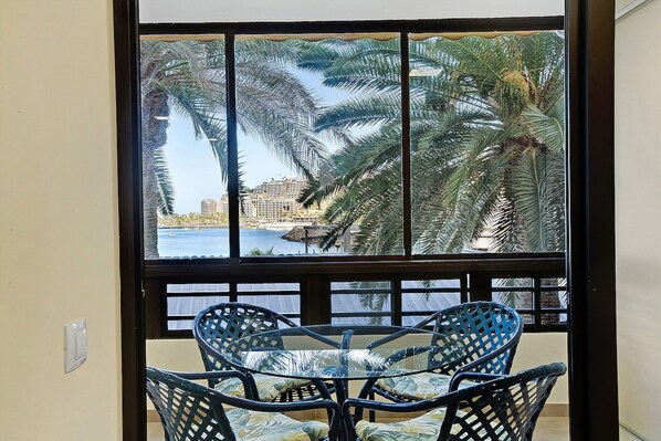 A room with a large window, a glass table, and two wicker chairs.