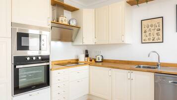 Una cocina con gabinetes blancos, horno de acero inoxidable, fregadero y cafetera.