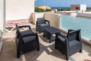 A rooftop terrace with wicker furniture, a pool, and a view of the sea.