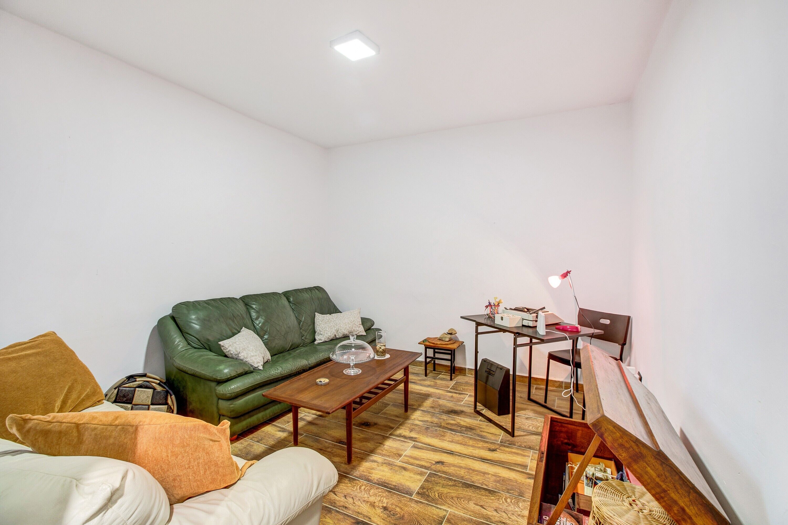 Un salon avec un canapé vert, une table basse en bois, une petite table d’appoint, une lampe et un fauteuil.