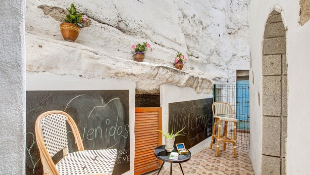 A rustic outdoor seating area with a wicker chair, a small round table with a plant, and chalkboard walls with graffiti. - Vacation Home 'Casa Bene' with Mountain View, Wi-Fi and Air Conditioning (Guimar)
