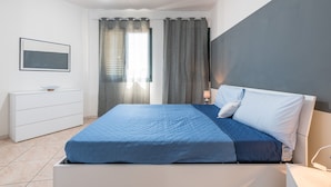 Una camera da letto con un letto, un comodino, una lampada, una cassettiera e un quadro appeso al muro.