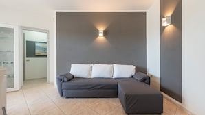 Un soggiorno moderno con un divano modulare grigio, una porta vetrata che dà su un balcone e un lampadario fissato al muro.