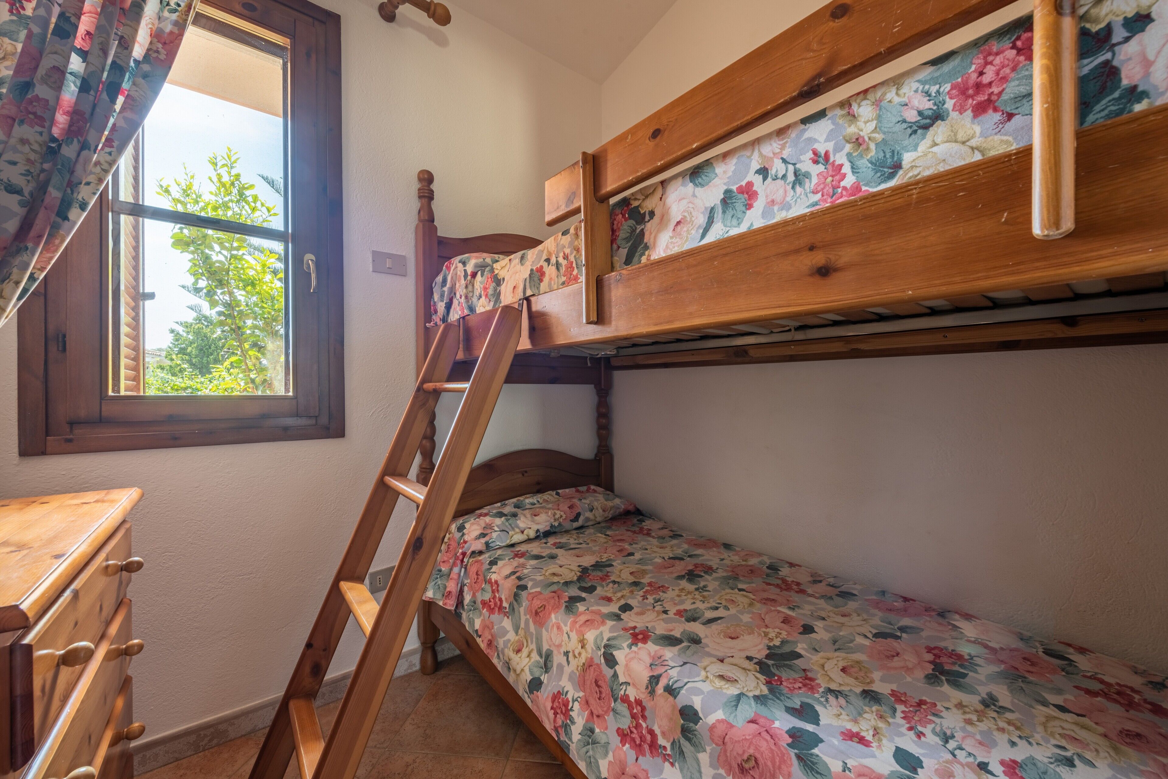 Ein Stockbett mit Blumenbettwäsche, ein Holztisch und ein Fenster mit Vorhängen.