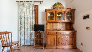 Een kamer met een houten kast, een televisie op een standaard, een stoel en een gordijn.