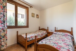 A bedroom with two wooden beds, a window with curtains, and a small table.