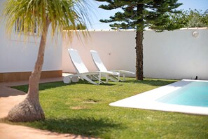 Ein Poolbereich mit zwei weißen Liegestühlen, einem kleinen Pool und einer Palme.