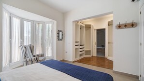 Un dormitorio con cama, una silla, un armario y un baño visible a través de una puerta abierta.