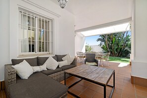 Ein Wohnzimmer mit einer Couch, einem Couchtisch, einem Fenster mit Jalousien und Blick auf den Garten.