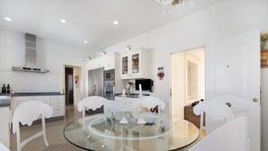 Una cocina moderna con armarios blancos, una mesa de comedor de vidrio y sillas blancas.