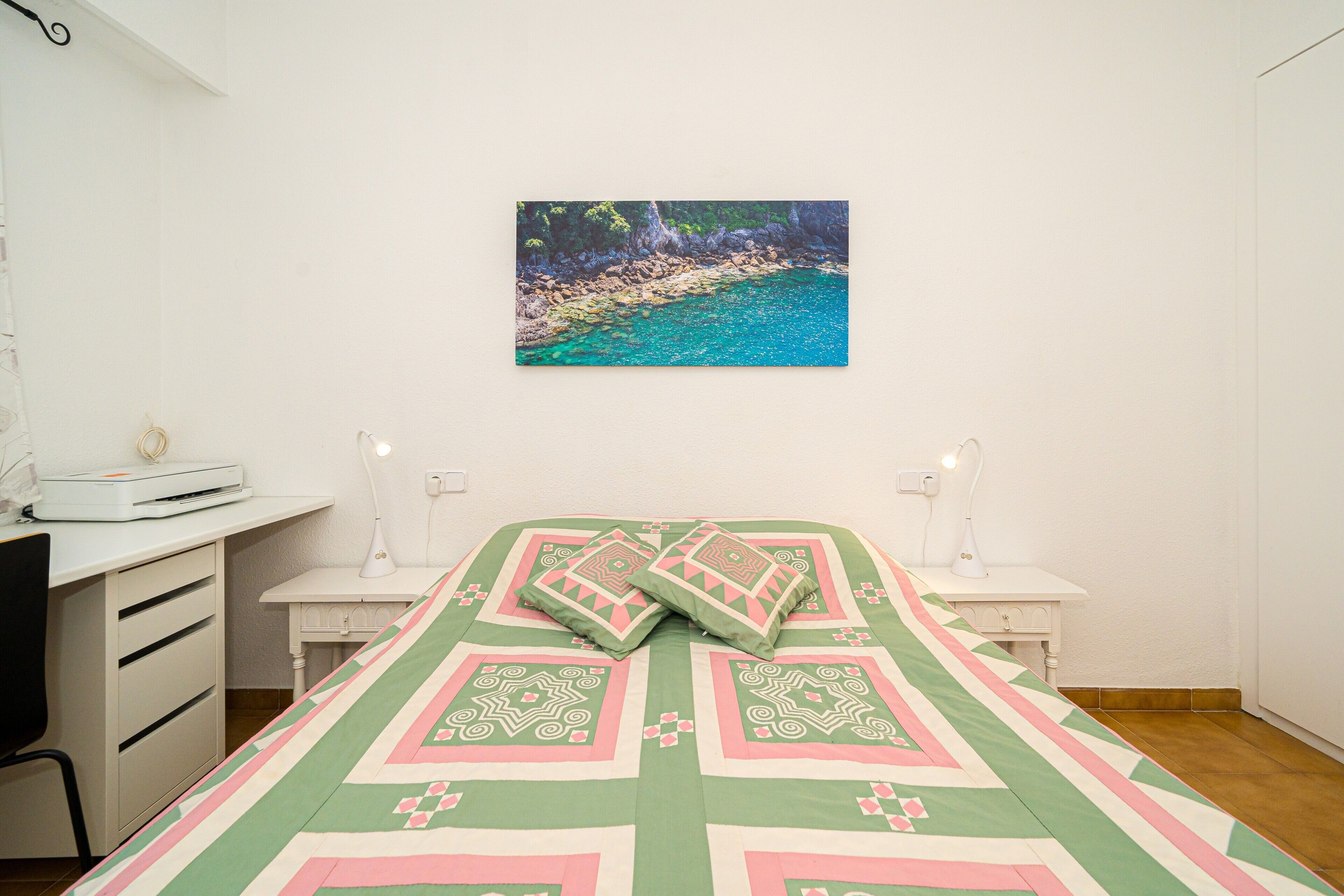 Une chambre à coucher comprenant un lit, un bureau, une chaise, une table de chevet et un tableau accroché au mur.
