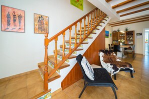 Een trap met houten spijlen, een eetgedeelte met een tafel en stoelen, en een boekenkast.
