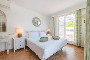 A bedroom with a bed, two bedside tables, a mirror, and a window with curtains.