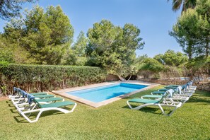 A rectangular swimming pool with a stone border, surrounded by a well-maintained lawn and a row of green lounge chairs.
