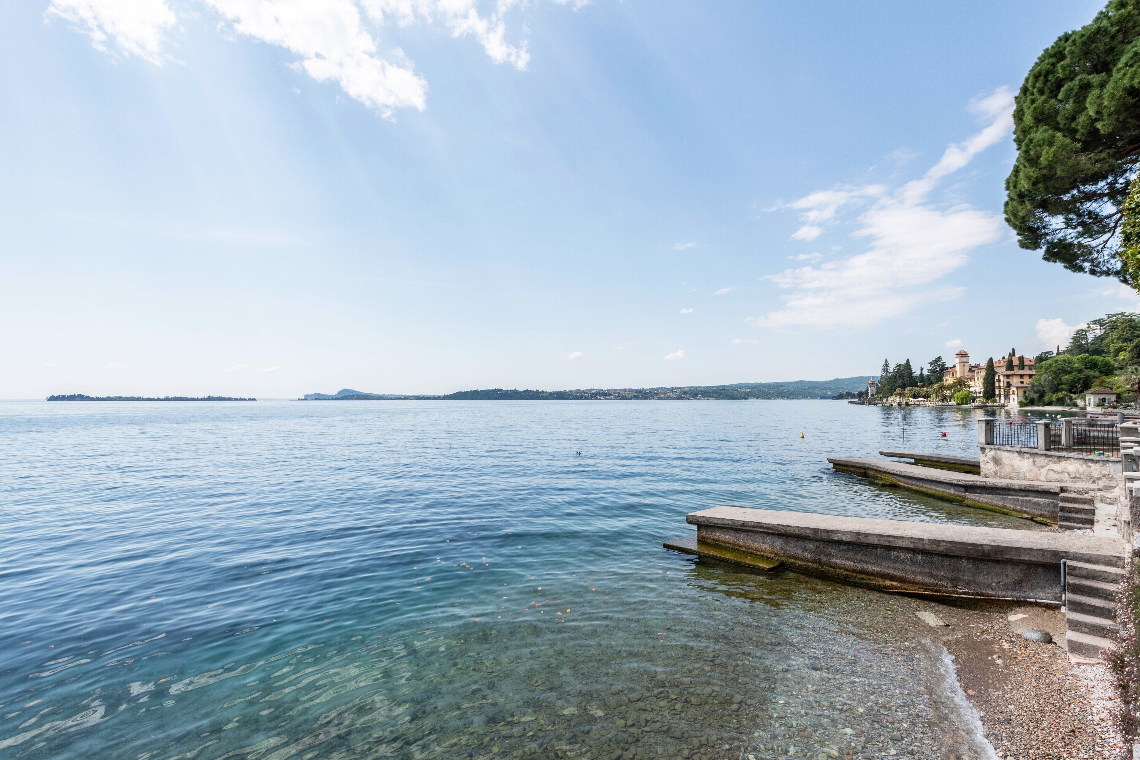 A waterfront view with clear water, a stone pier, and buildings in the background.