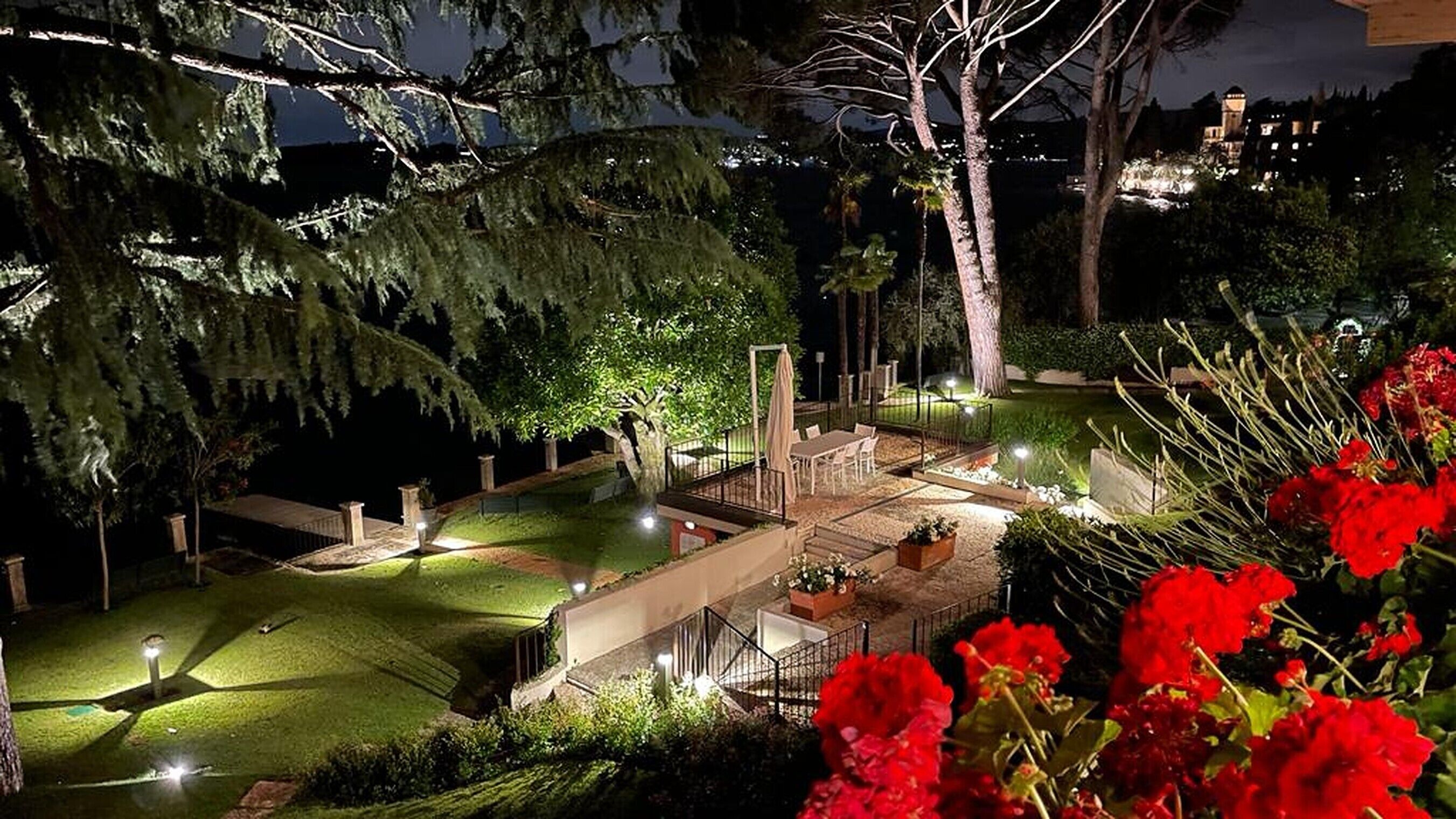 Un'area esterna ben illuminata con un tavolo e sedie, circondata da alberi e un piccolo elemento d'acqua.