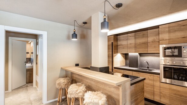 Een moderne keuken met houten kastjes, een roestvrijstalen oven en een bar met barkrukken.