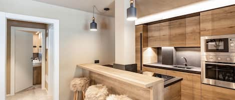 Eine moderne Küche mit Holzausstattung, einem Edelstahlbackofen und einer Bar mit Hockern.