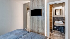 Een slaapkamer met een bed, een wandgemonteerde televisie en een badkamer met een wastafel en spiegel.