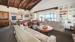 Un vaste salon doté d’un haut plafond, d’une grande fenêtre donnant sur la plage et d’un coin salon confortable avec une table basse ronde.