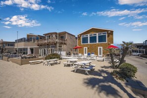 A beachfront property with a two-story building, outdoor seating, and a sandy patio area.