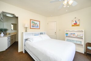 A bedroom with a bed, bedside table, lamp, and a wall with a framed picture and a sign.