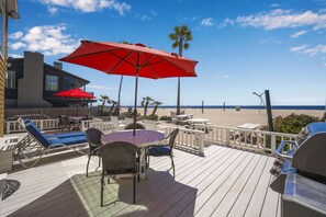 A wooden deck with outdoor seating, including chairs and tables, and a red umbrella.