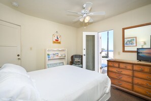 A bedroom with a bed, a dresser, a shelf with books, a ceiling fan, and a door leading to a balcony.