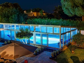 A modern glass-enclosed pool area with a stone pathway leading to a seating area.