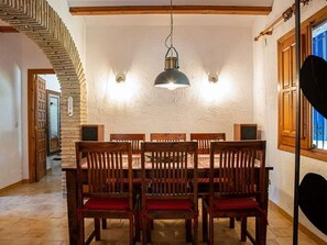 Zona pranzo con parete in mattoni, sedie di legno con cuscini rossi, lampadario e una scala in legno.
