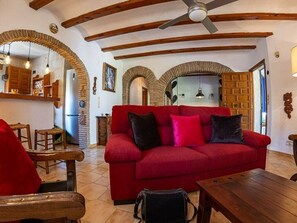 Un divano rosso, mobili in legno, una ventola a soffitto e travi a vista.