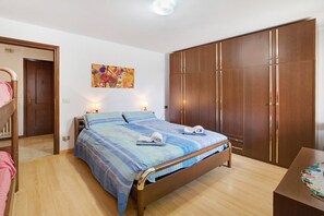 A bedroom with a bed, bedside lamps, a wardrobe, and a painting on the wall.