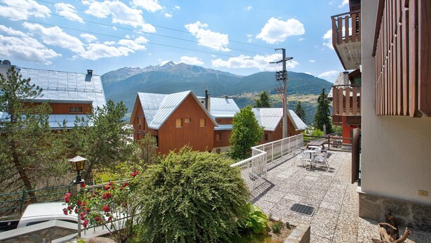 Ein Wohngebiet mit Häusern, einem Balkon mit Gartenmöbeln und einem Berg im Hintergrund.