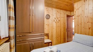 Ein Zimmer mit Holzwänden, einem Bett, einem Sessel und einem Kleiderschrank.