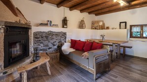 Un intérieur rustique avec une cheminée en pierre, des poutres en bois, un canapé avec des coussins rouges et une table en bois.