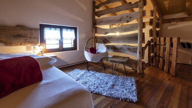 Une chambre confortable avec un plafond en bois, un lit, une chaise et une fenêtre.