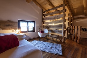 Ein gemütliches Schlafzimmer mit Holzbalkendecke, einem Bett, einem Sessel und einem Fenster.