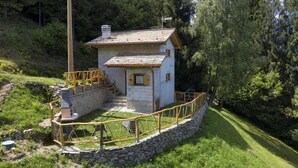 Un petit bâtiment blanc avec un escalier en pierre, une terrasse en bois et un mur de pierre qui entoure la propriété.