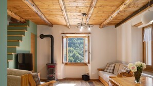 A cozy room with a wooden ceiling, a sofa, a dining table, and a window with a view of trees. - Apartment 'Bellavista' with Mountain View & Garden (Chiesa In Valmalenco)