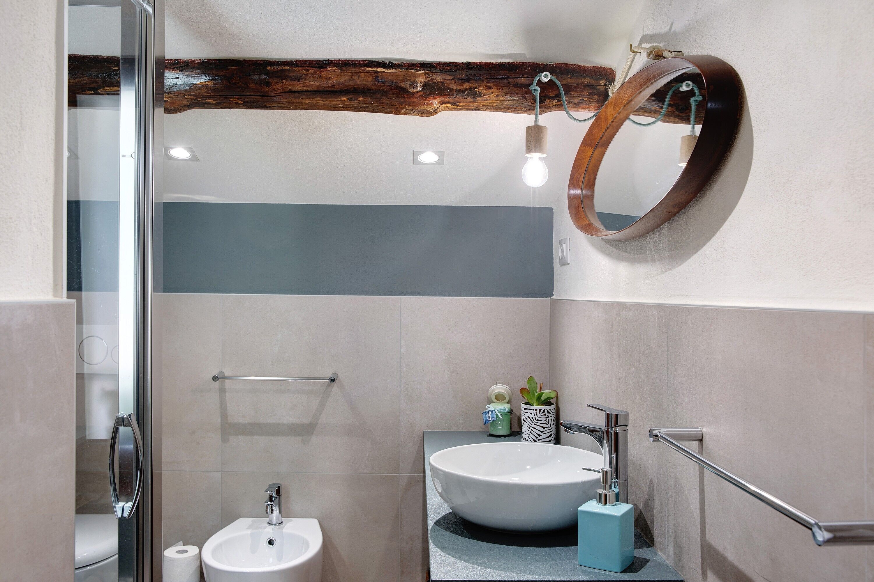 A bathroom with a large mirror, a sink, a towel rack, and a wooden beam on the ceiling.