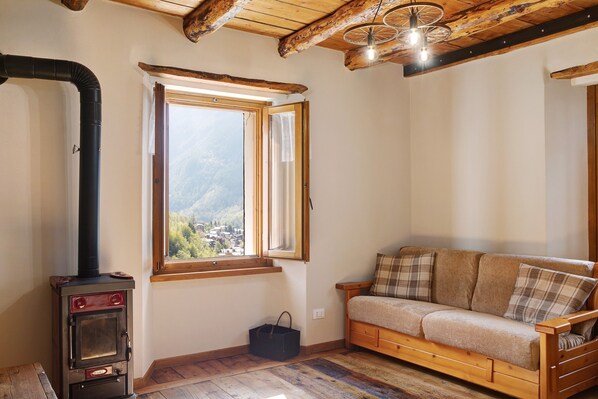 A cozy room with a wooden sofa, a fireplace, a window with a view, and a ceiling with exposed beams.